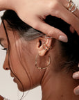 Noele large gold hoop earrings by PIERETTI worn on ear, sculptural wave hoops for modern styling