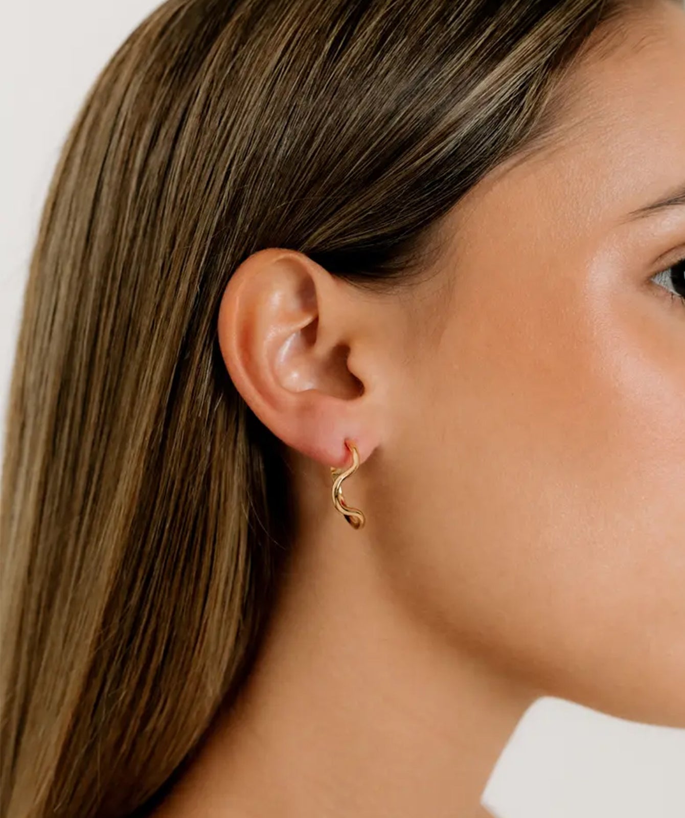 Noele gold wave hoop earrings by PIERETTI worn on ear, medium sculptural hoops for everyday styling