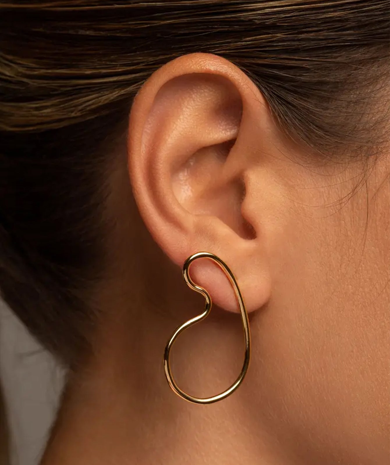 Naty gold drop earrings by PIERETTI worn on ear, sculptural curved earrings for modern styling
